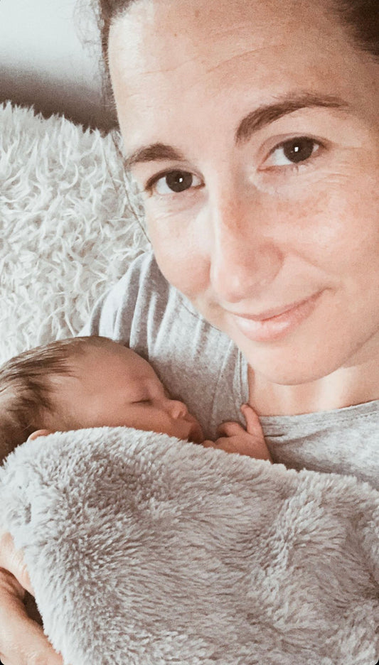 mum-smiling-at-camera-with-sleeping-baby-in-arms-under-furry-blanket-bon-and-bear