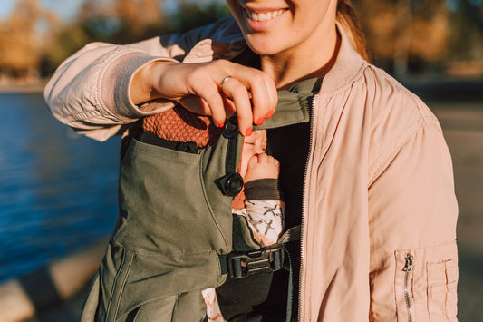 mum-similing-holding-strap-on-baby-carrier-with-sleeping-baby-bon-and-bear