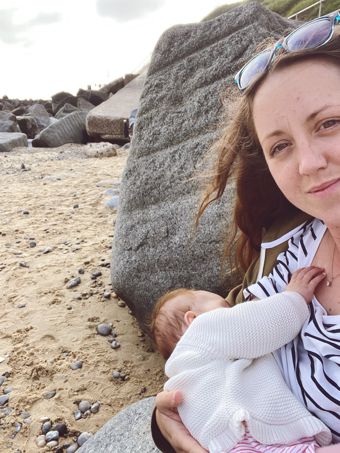 mum-sat-on-beach-breastfeeding-baby-in-striped-breton-top-smiling-at-camera-bon-and-bear