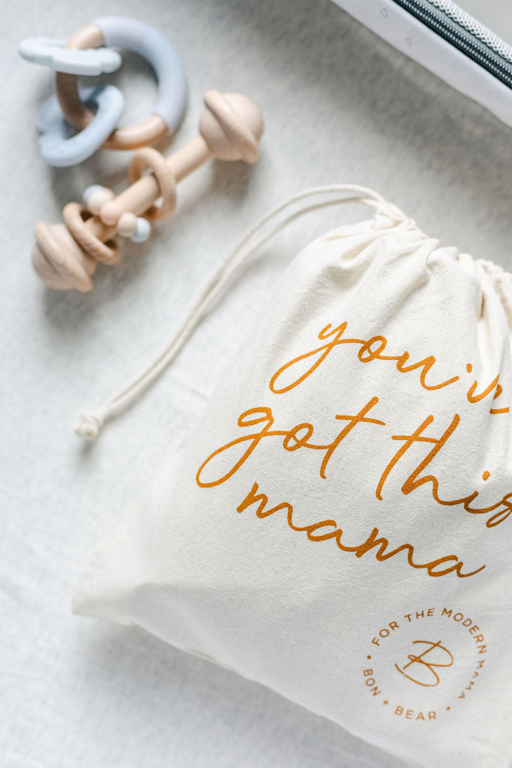 canvas-drawstring-bag-with-youve-got-this-mama-logo-next-to-baby-rattle-and-baby-teether-bon-and-bear